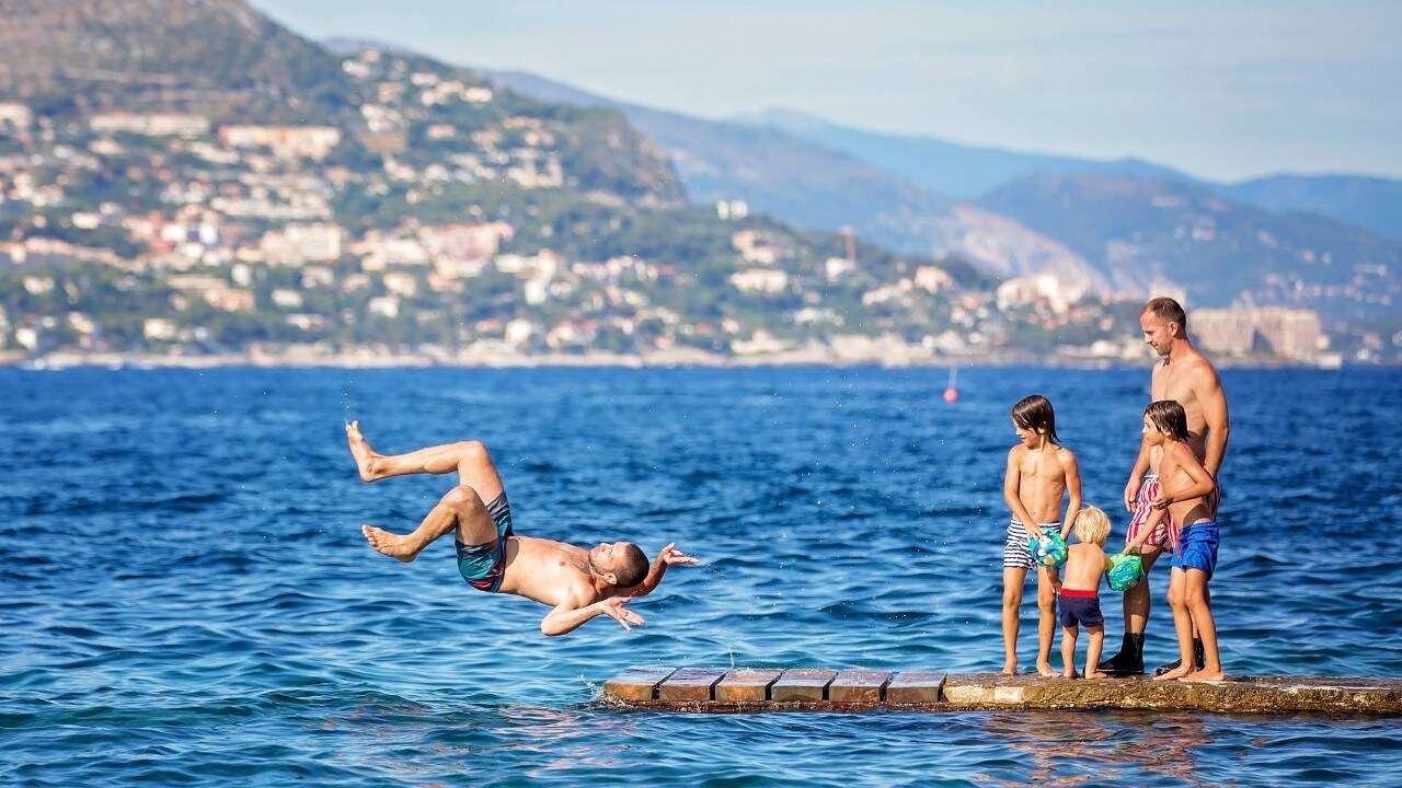 Happy group of people, children and adults, jumping in the water off dock, splashing and having lots of fun