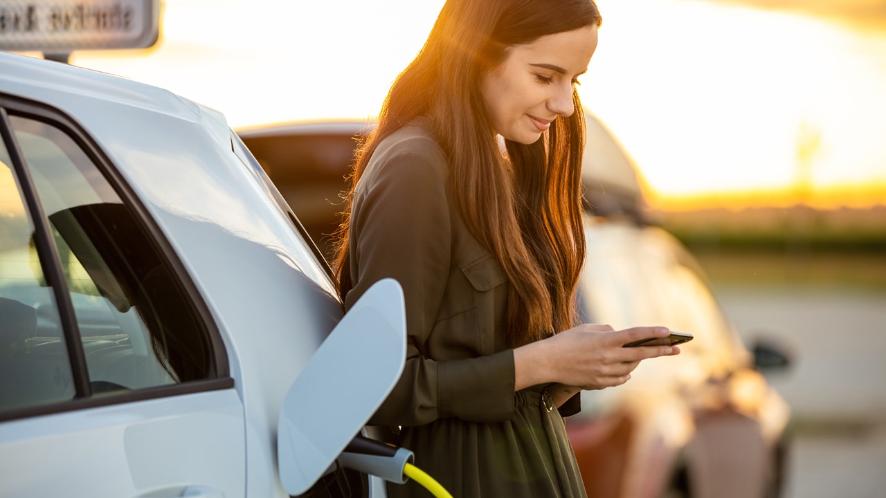 Mujer cargando un vehículo eléctrico mientras habla por teléfono.