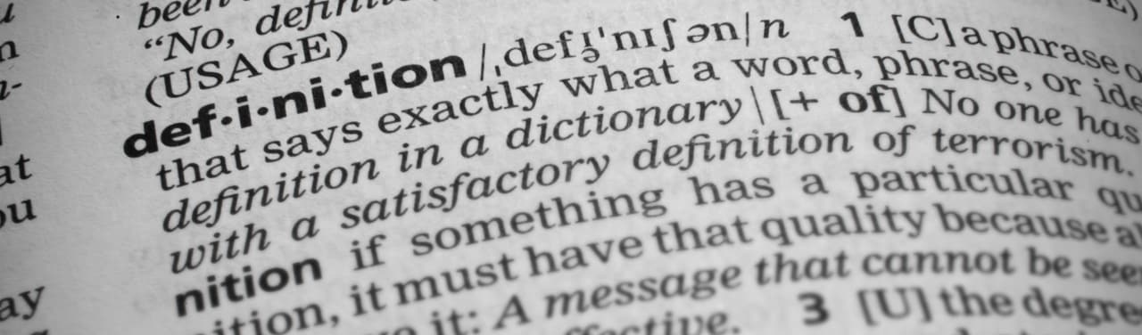Primer plano de la definición de la palabra en un diccionario. La página se curva y tiene un efecto viñeteado o quemado en los bordes donde las esquinas son más oscuras. Se centra en la definición de la palabra.